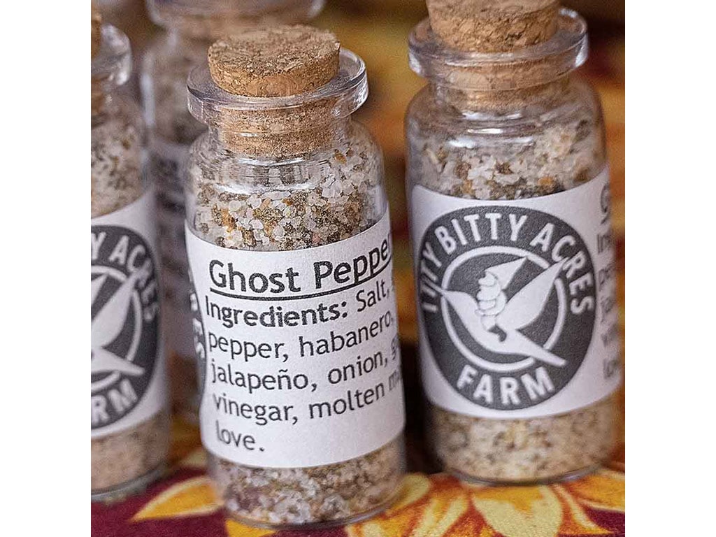 Close-up of glass spice jars labeled "Ghost Pepper" with ingredients like salt, peppers, and spices, from Litty Bitty Acres Farm.