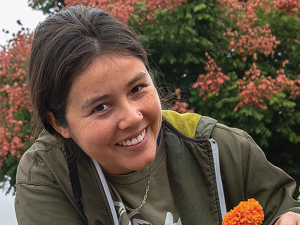 A person in a green jacket holds a vibrant orange flower.