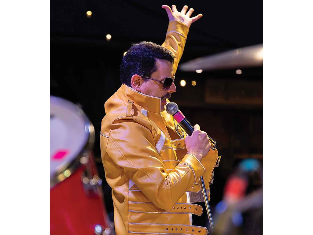 A performer in a vibrant yellow jacket passionately sings into a microphone.