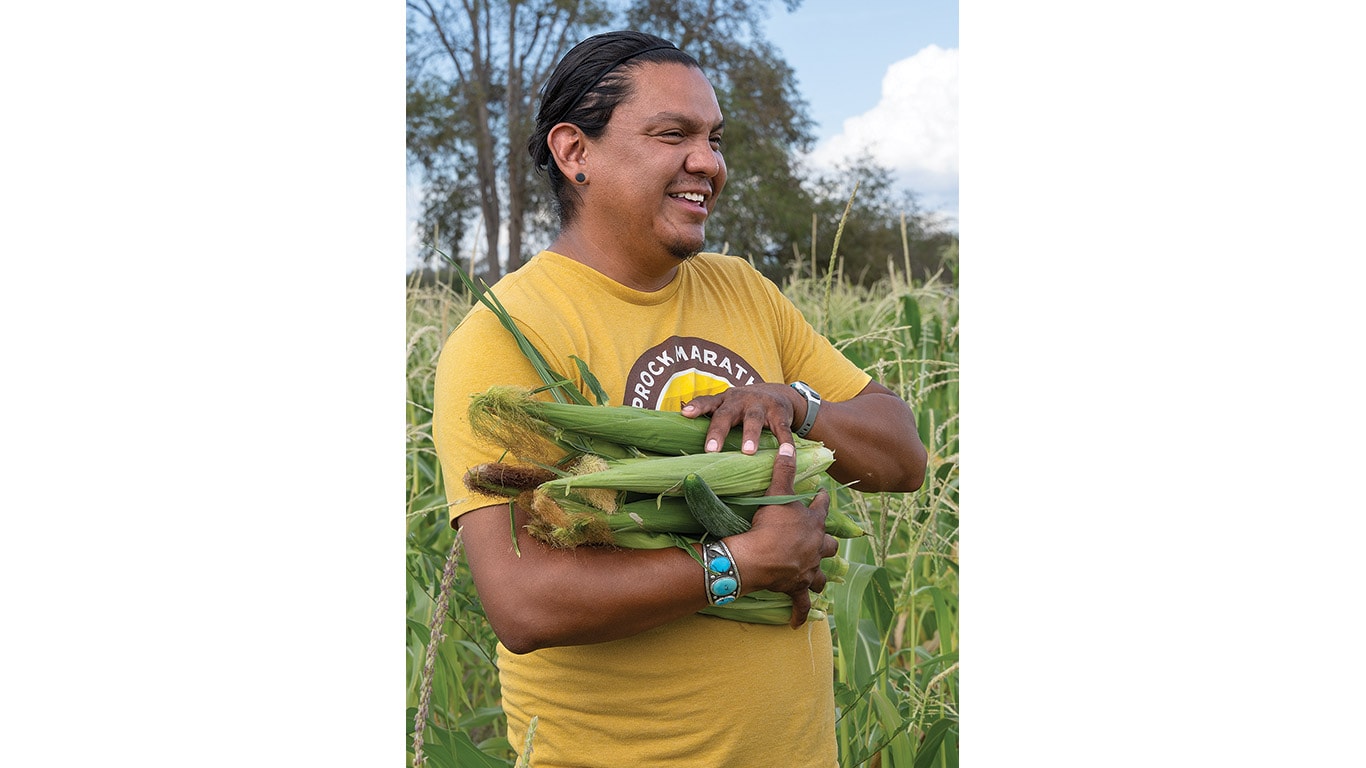 Person smiles while holding freshly harvested corn in a field.