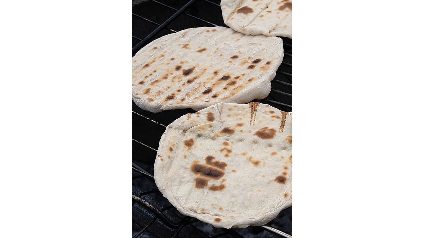 Flatbreads cook on a metal grill grate.