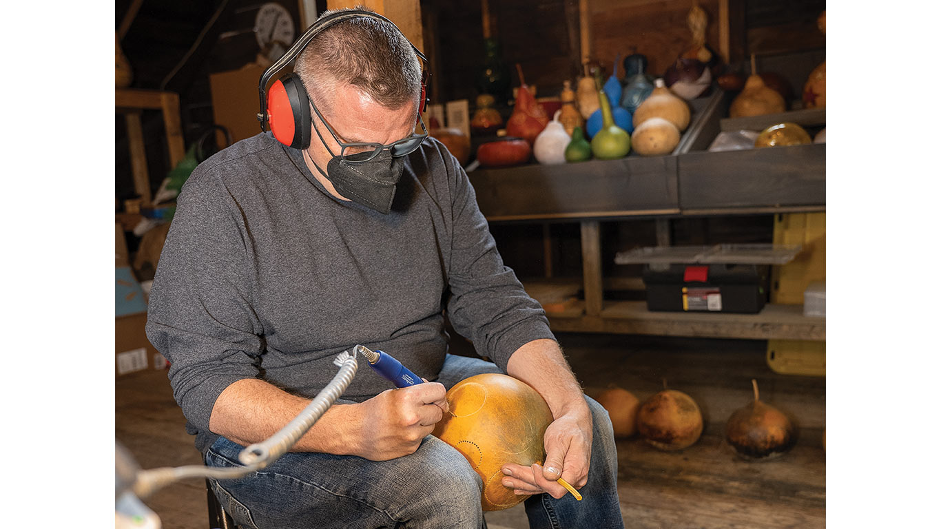 Man wears safety gear while carving a dried gourd indoors.