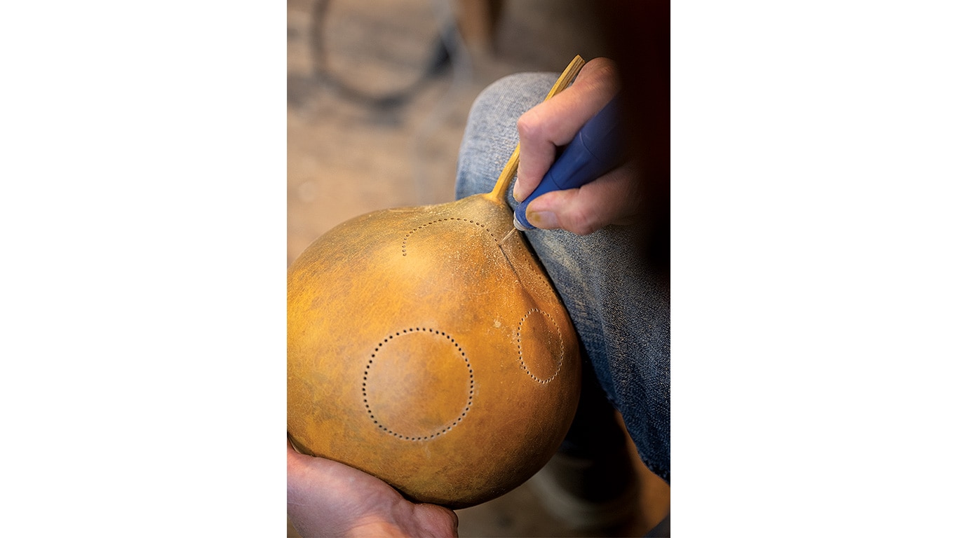Close‑up of hands carving circular patterns into a gourd.