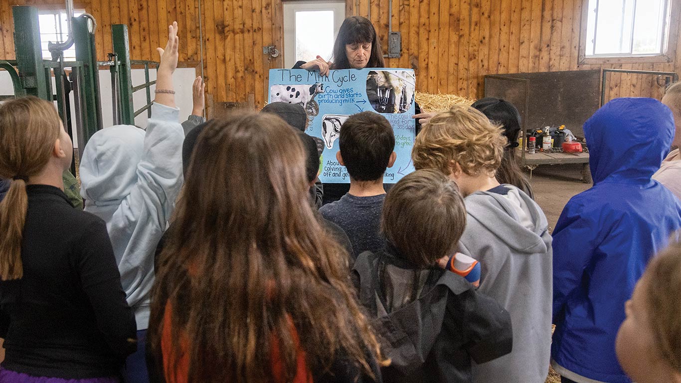 Adult holds an illustrated poster while children listen inside a barn.