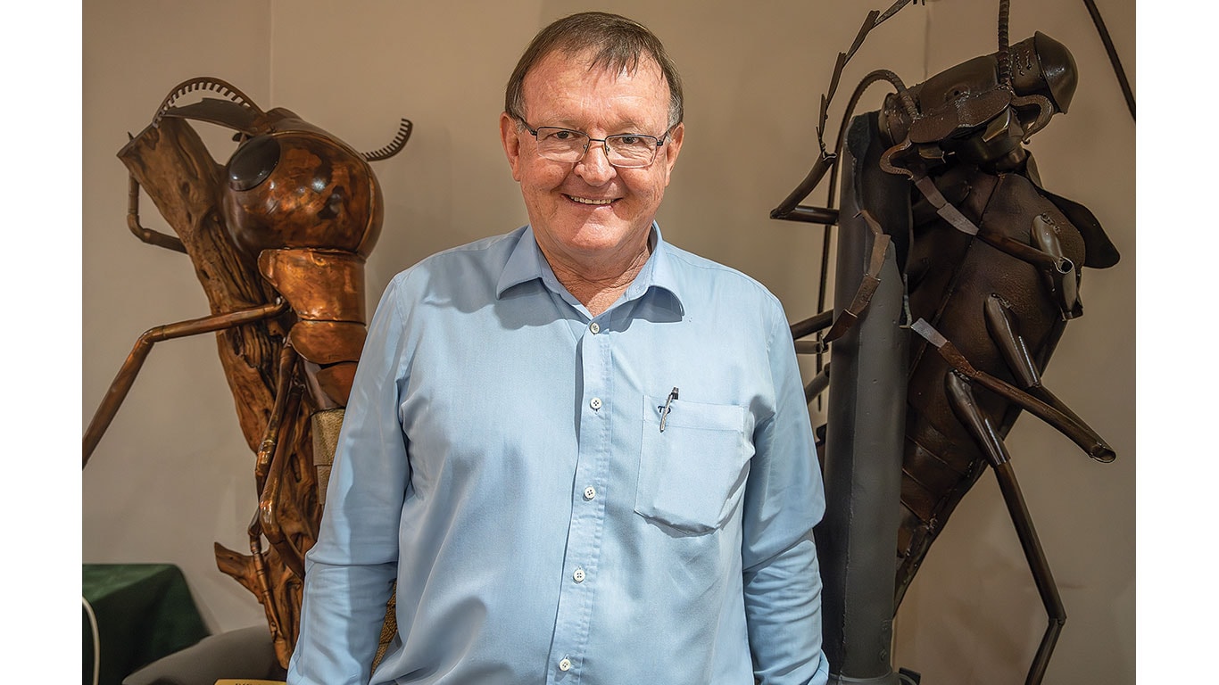 A smiling person stands between two large beetle sculptures indoors.