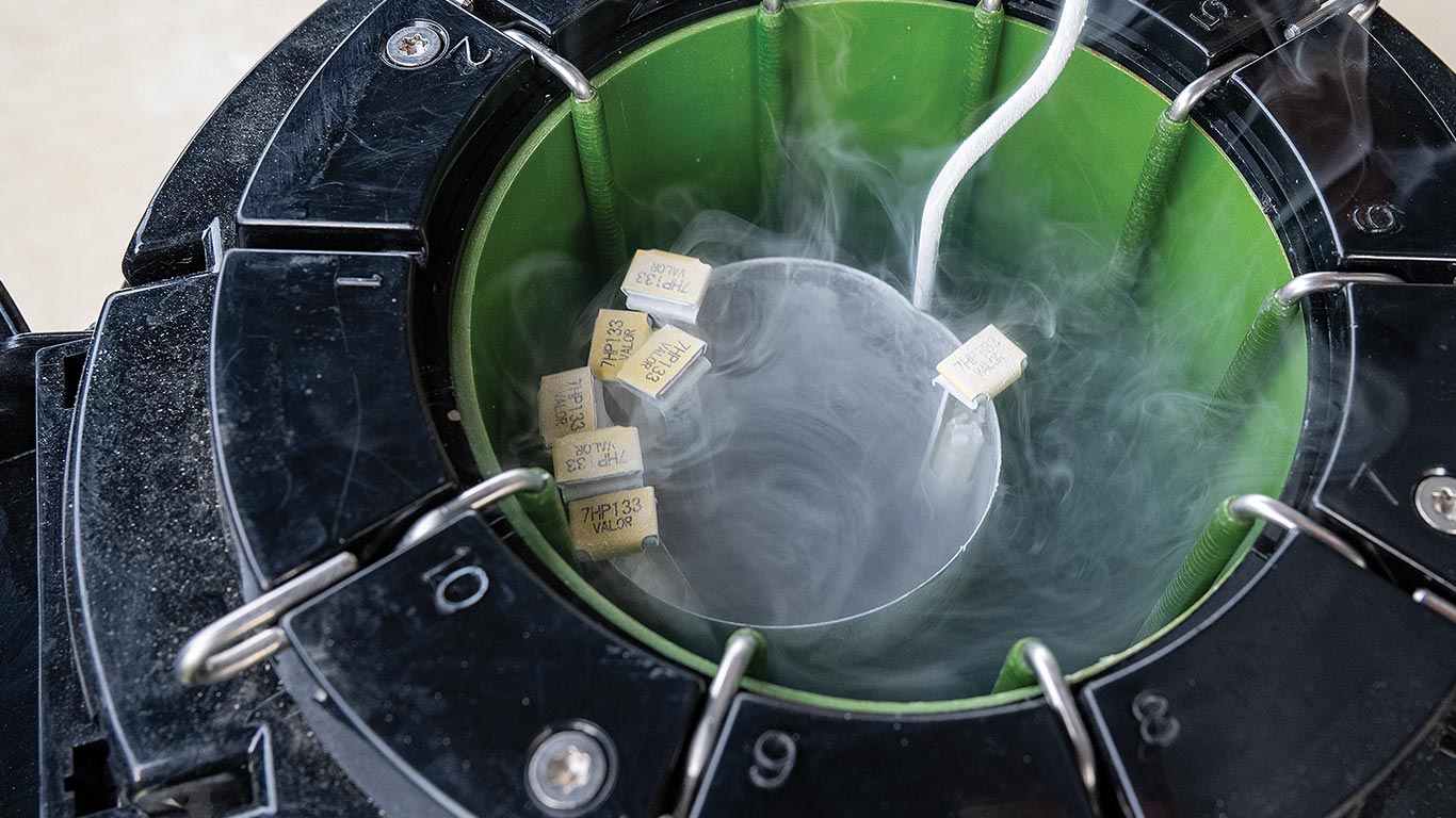 A cryogenic storage container releasing vapor, holding several labeled samples on a suspended metal holder.
