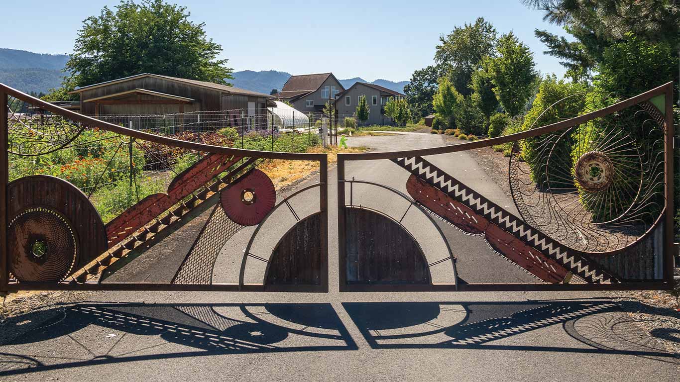 Decorative metal gate with geometric patterns at the entrance of a rural property.