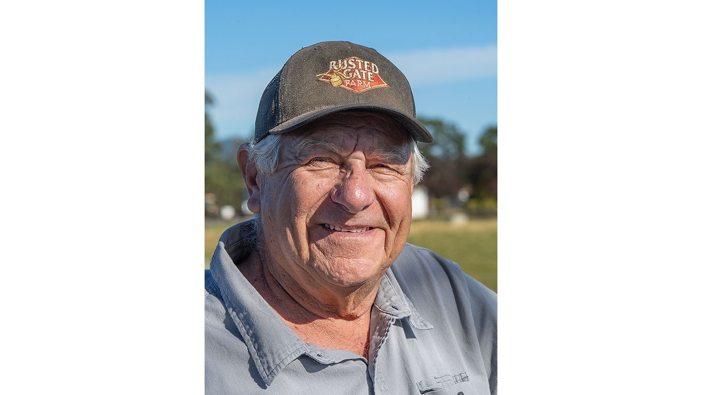 Person wearing a gray collared shirt and a dark cap with “Rusted Gate Farm” logo outdoors.