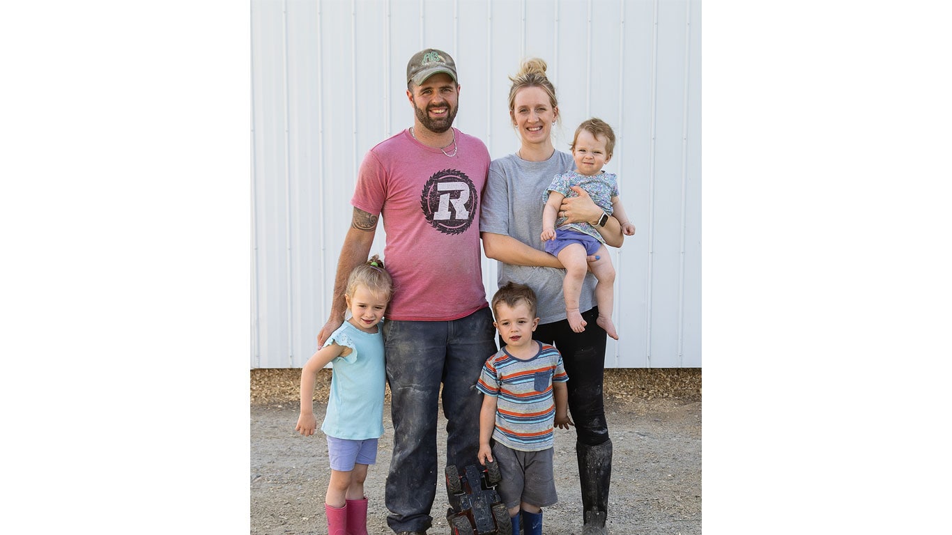 Two adults and three children standing together outside near a white wall.