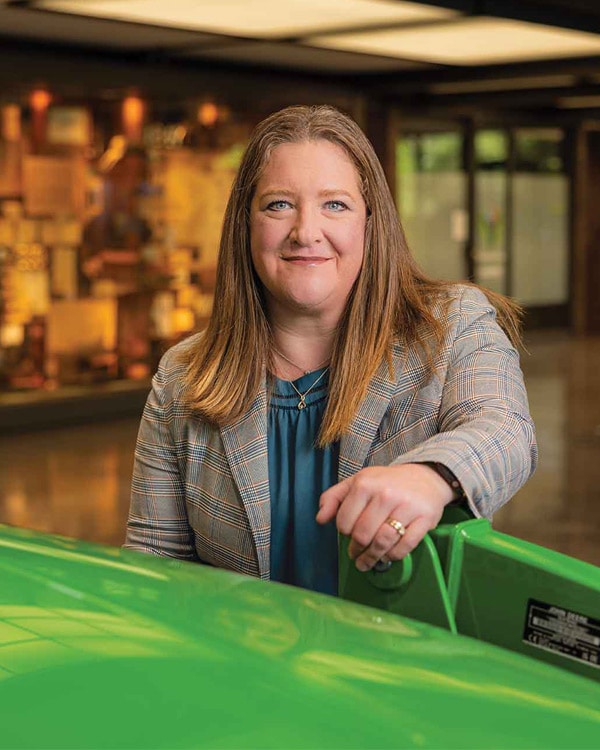Person standing behind a green tractor in an indoor showroom with displays in the background.