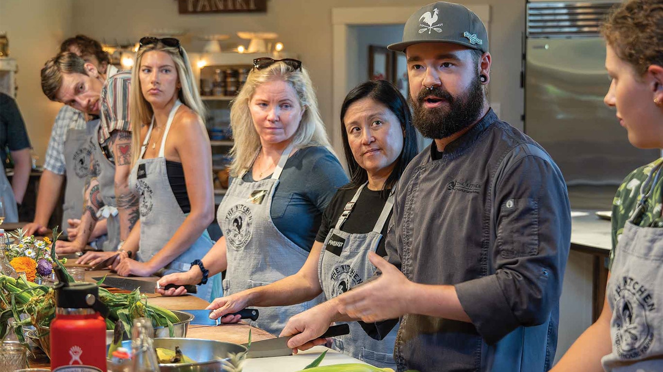 A group of people standing around a kitchen workspace, wearing aprons and preparing ingredients.