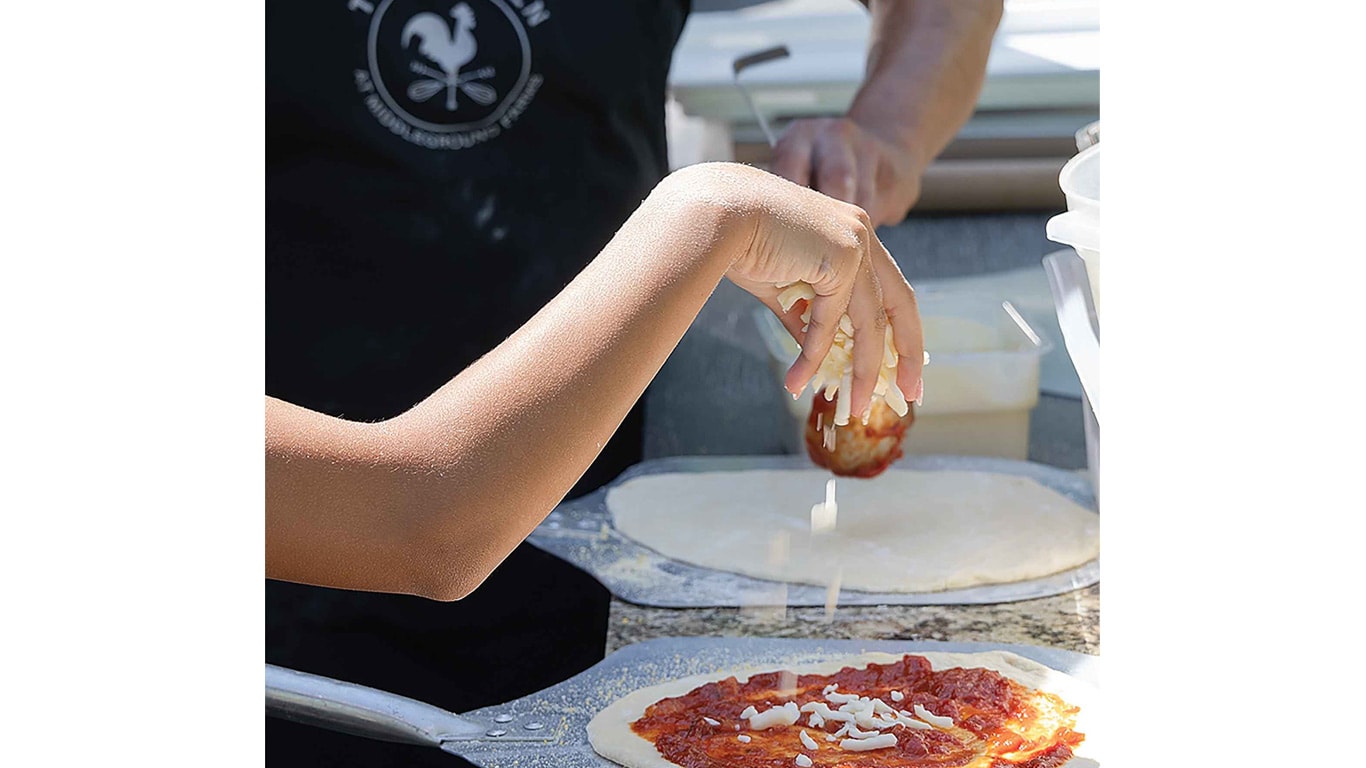 Close-up of a hand sprinkling cheese onto a pizza with sauce.
