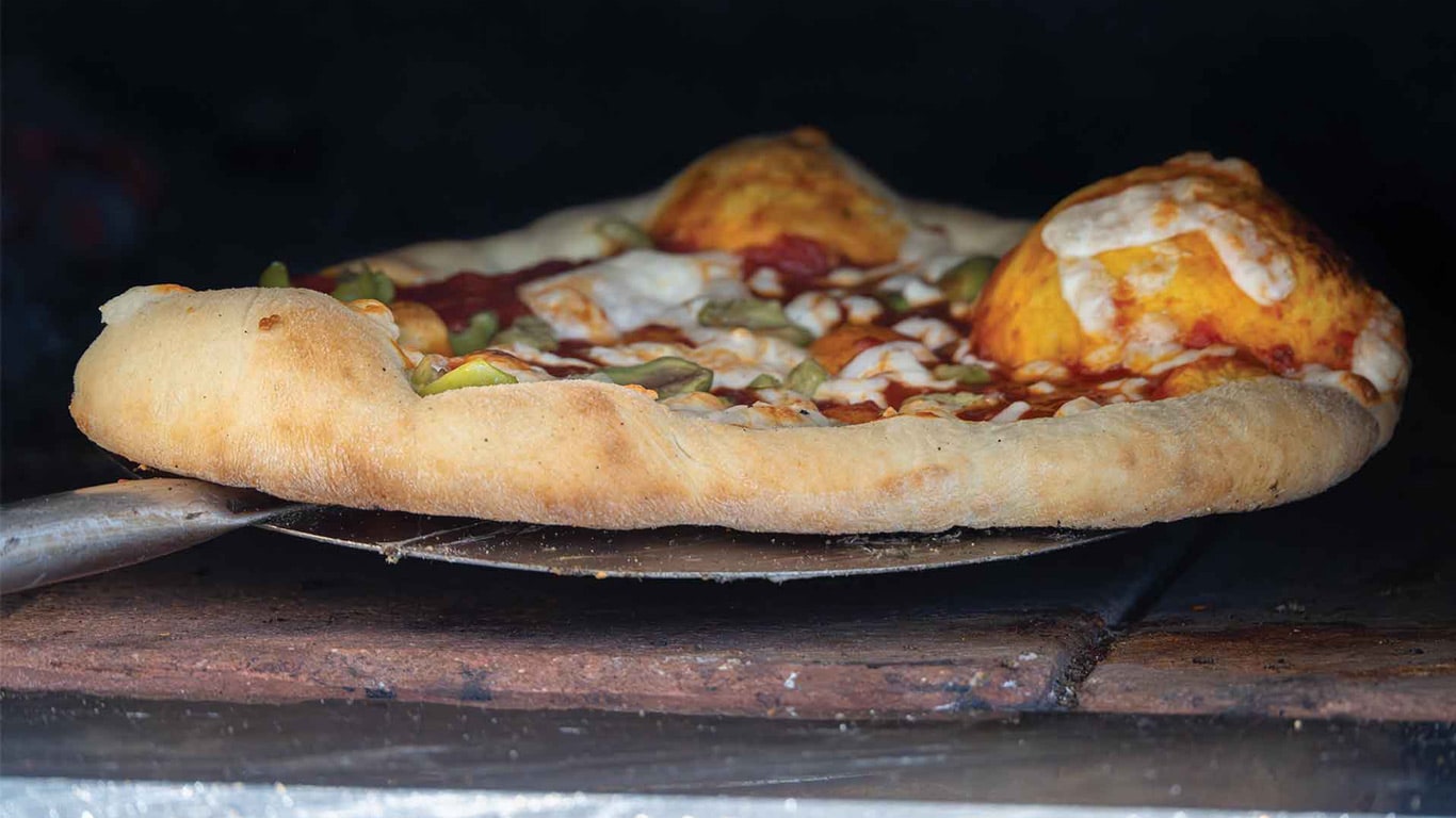 Freshly baked pizza being removed from an oven.