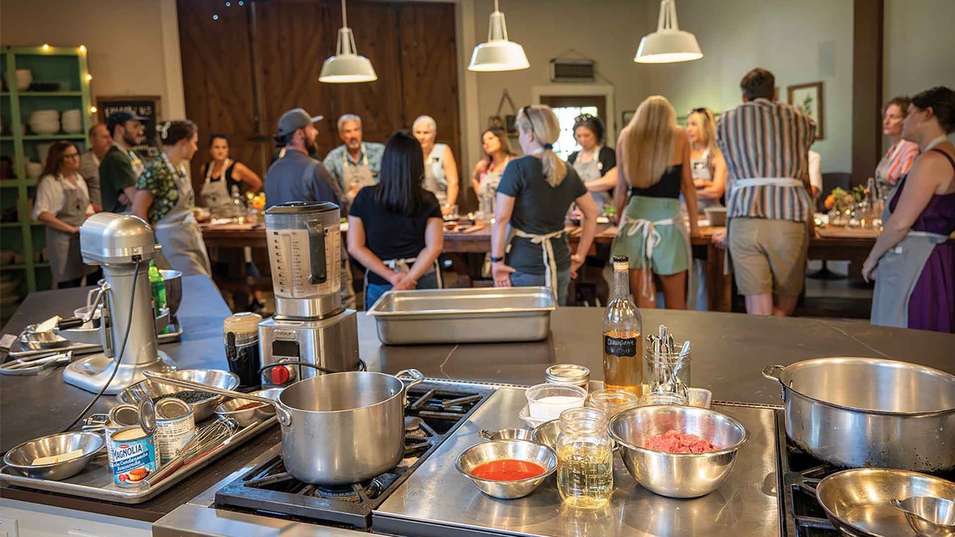Group cooking class gathered around tables in a kitchen studio.