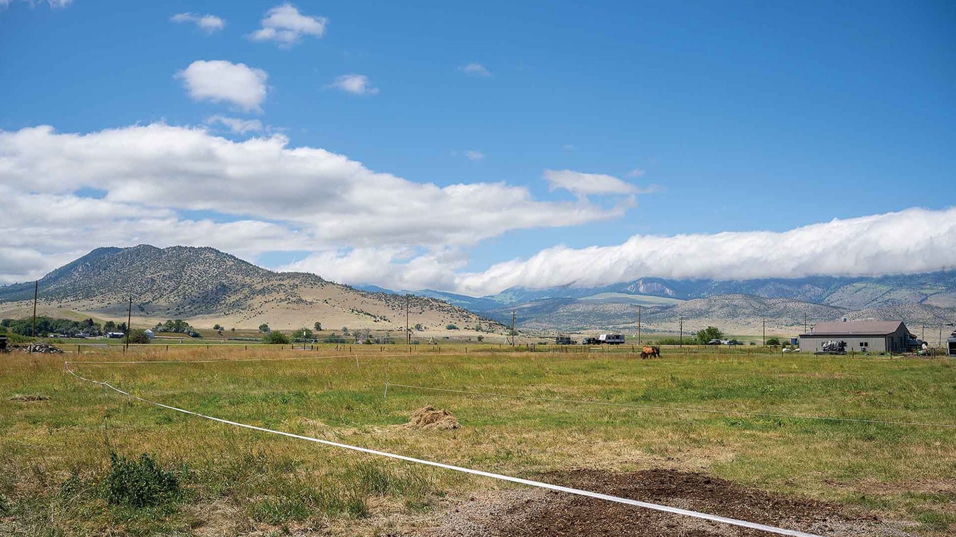 Wide view of an open field with mountains, clouds, and a long measuring tape stretched across the grass.