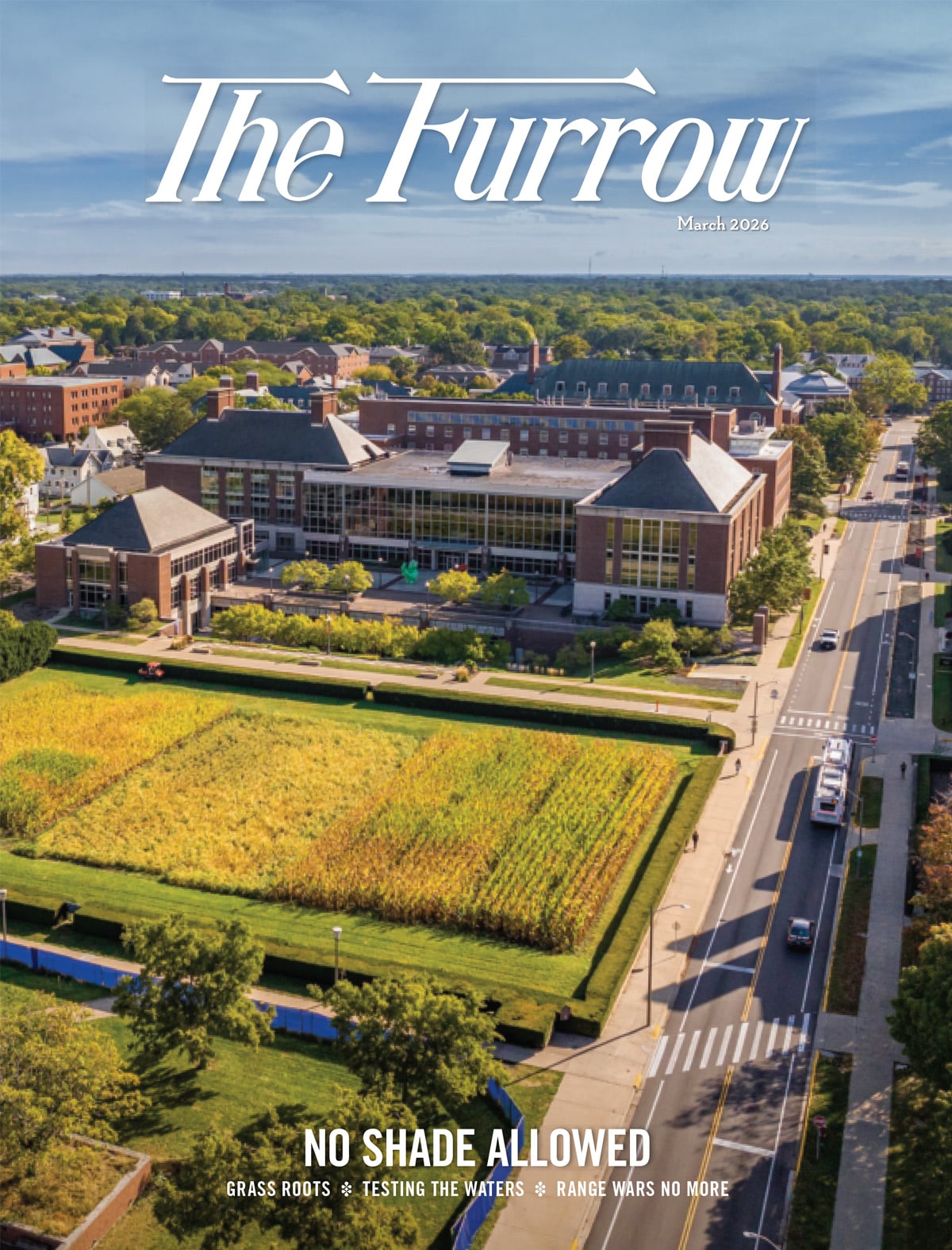 Aerial view of a university campus with academic buildings, a street, and a crop field surrounded by trees.