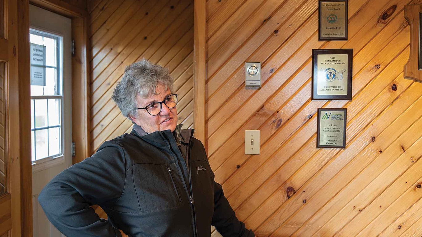 Person standing indoors near a wood-paneled wall with award plaques.