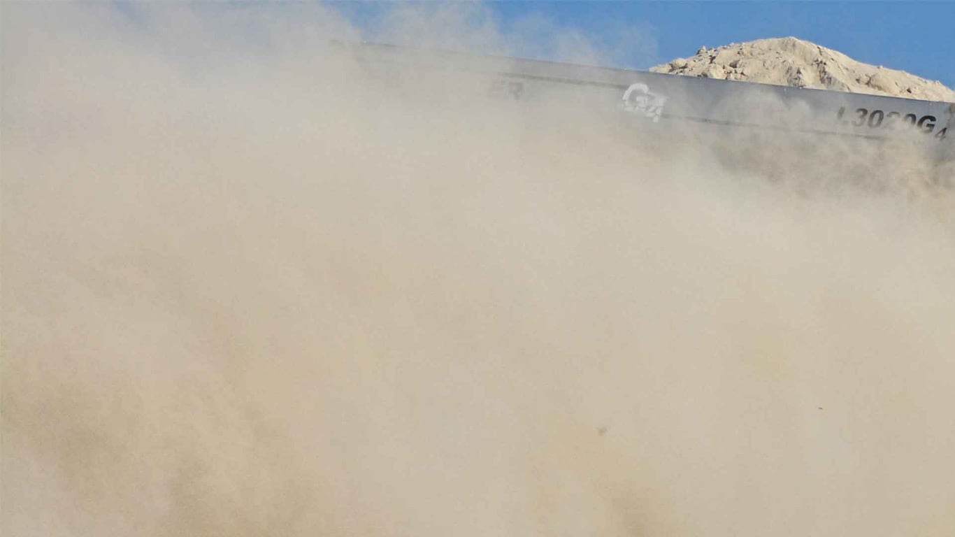 Large cloud of dust rising near a mound of light-colored material.