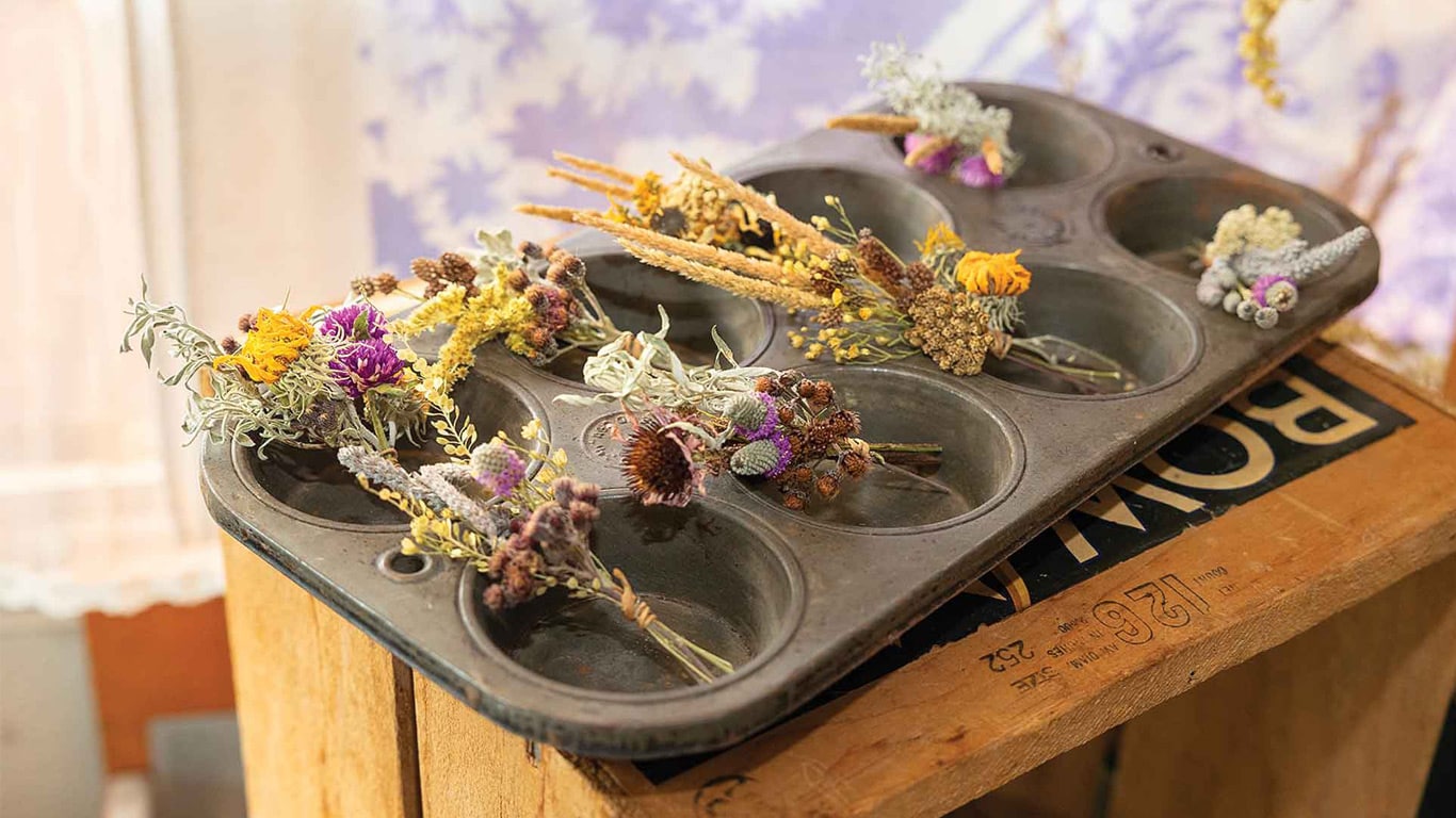 Dried flower bundles arranged in a metal muffin tin resting on a wooden crate display.