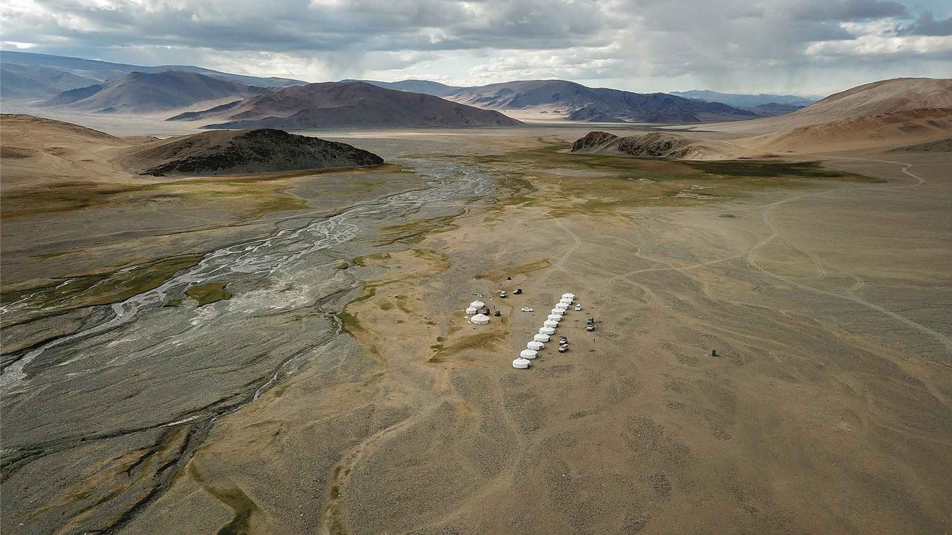 Aerial view of a remote valley with clustered white yurts on open desert terrain.