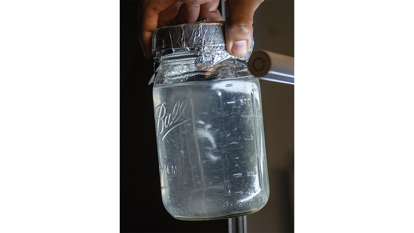 Jar with foil cover connected to tubing, held by a hand.
