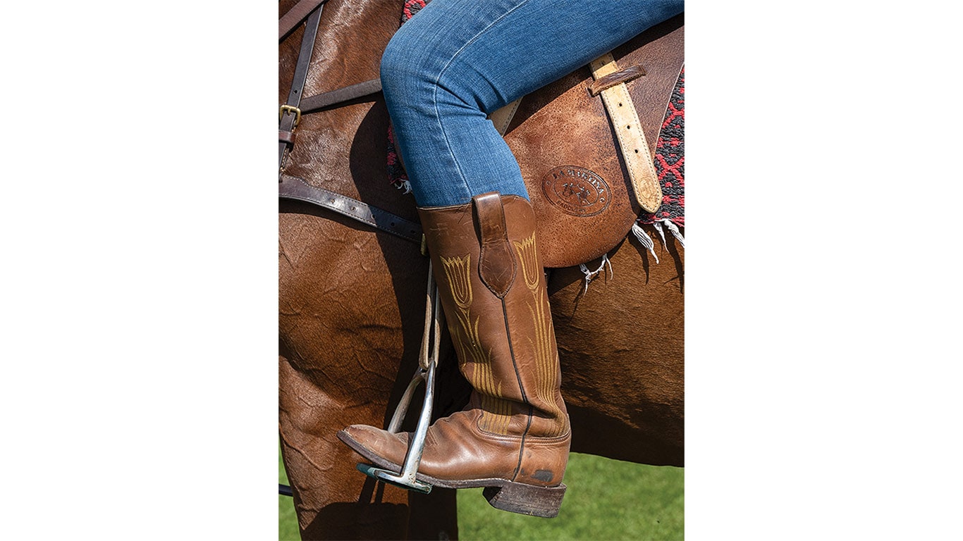 Close-up of a rider's boot in a stirrup on a saddled horse.