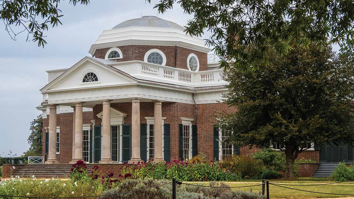 Neoclassical brick building with columns, dome roof, and garden in front framed by trees.