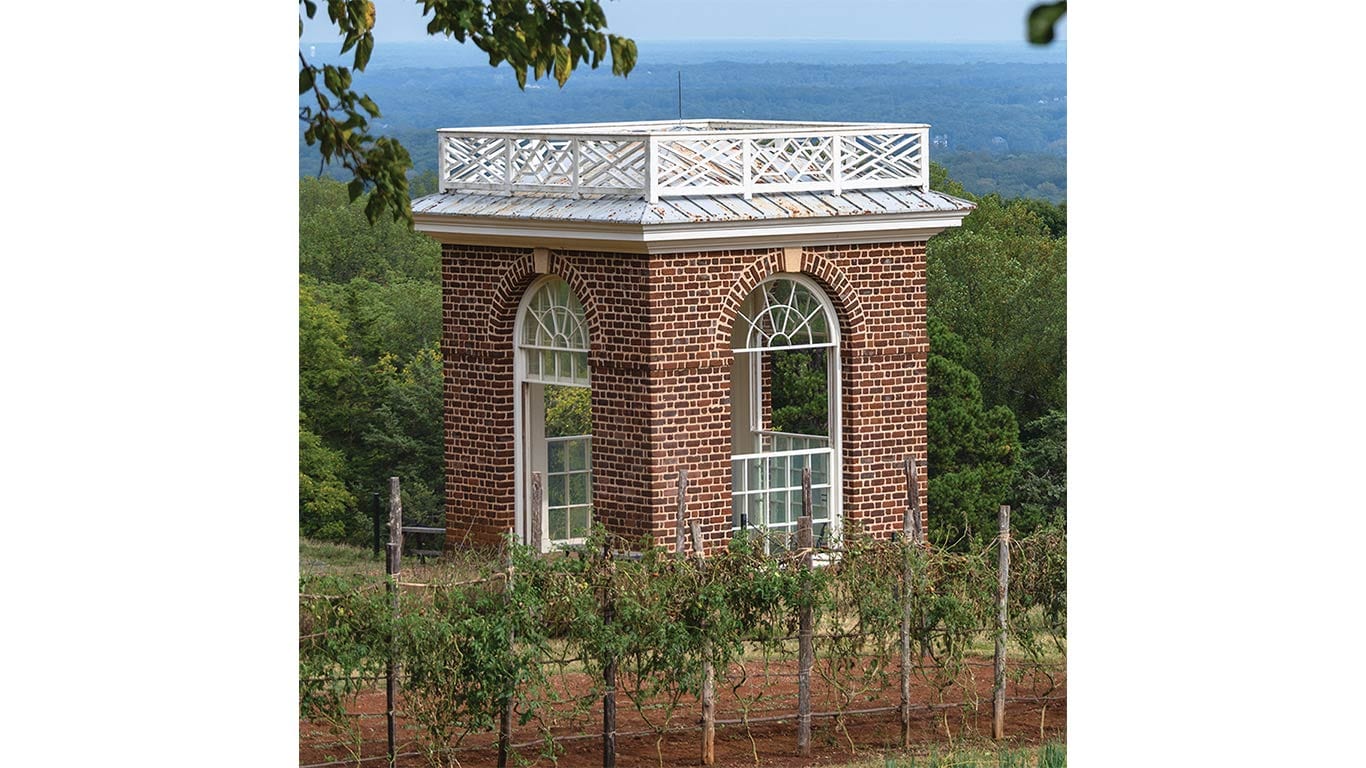Small brick pavilion with arched windows overlooking a vineyard and landscape.