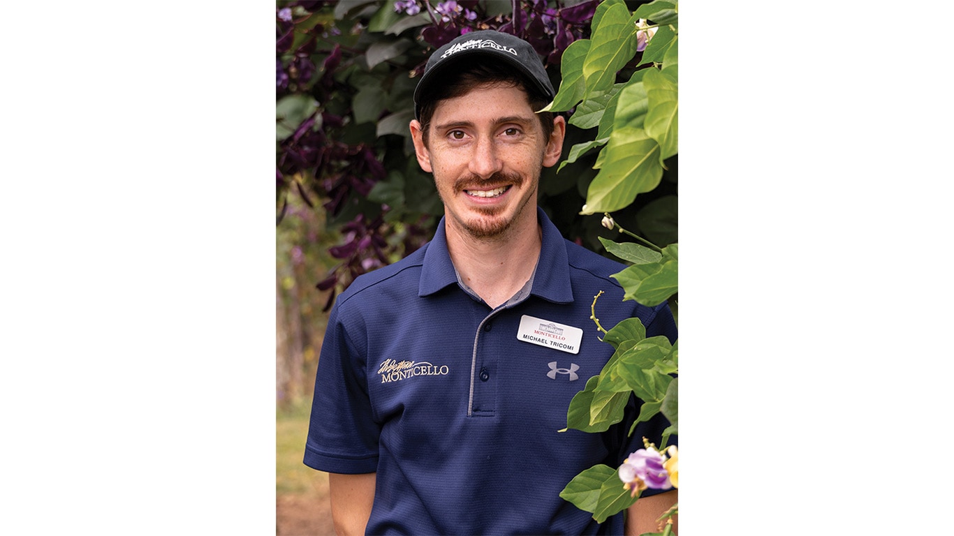 Person wearing a "Monticello" shirt and name tag standing beside leafy plants.