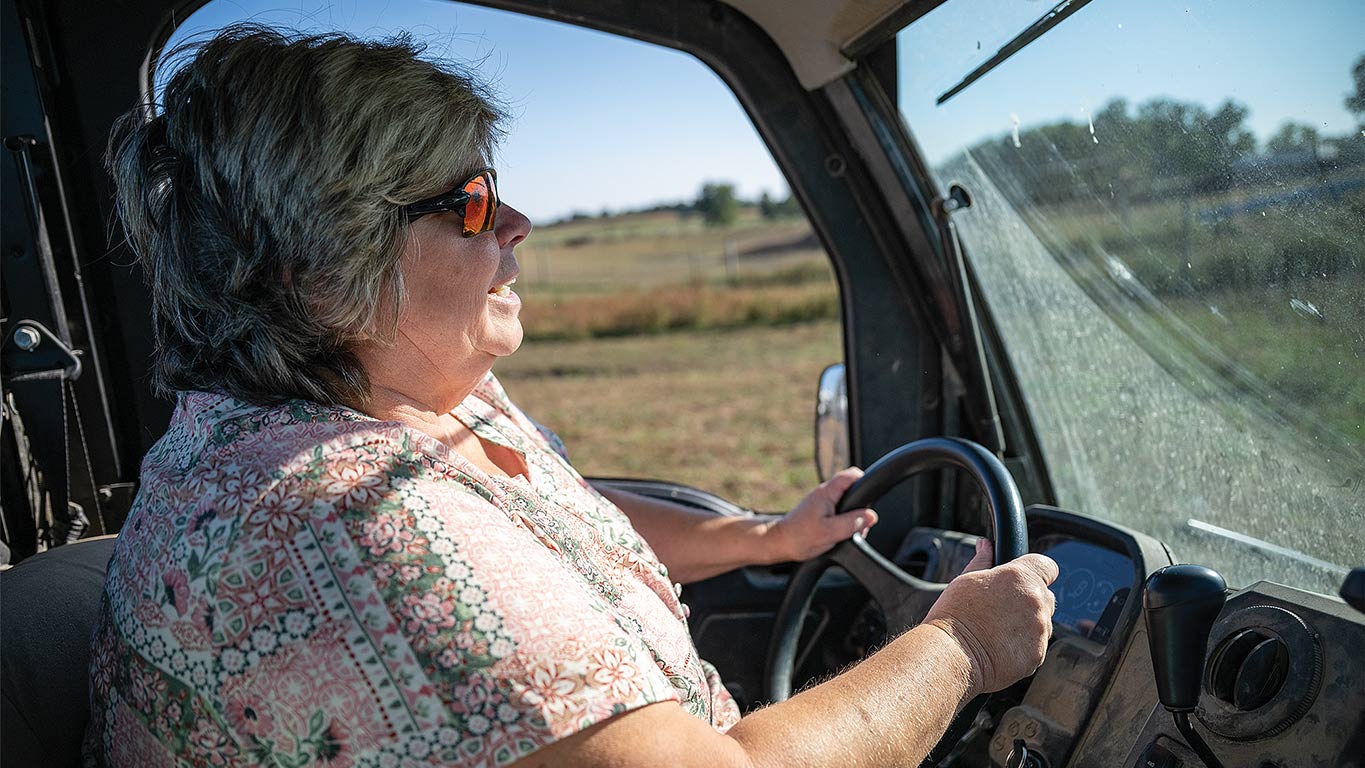 Person driving a utility vehicle across a rural field.