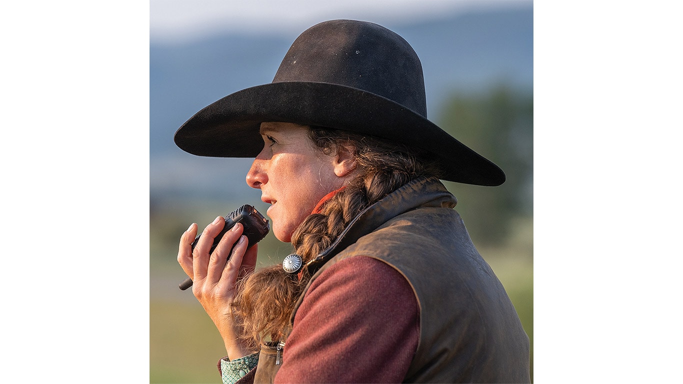 A person with a cowboy hat on speaking into a walkie talkie with the sun in their face.