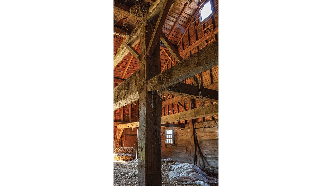 Interior of a wooden barn with exposed beams, hay, and a small window letting in light.