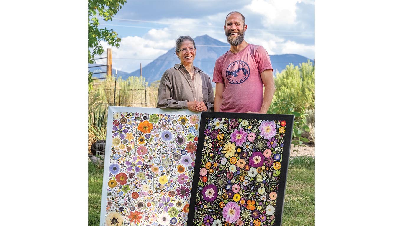 Two people standing outdoors displaying framed pressed flower artwork.