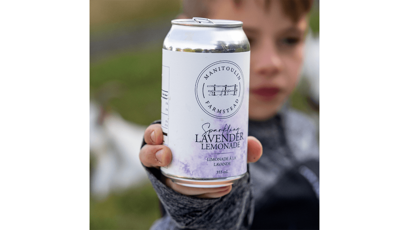 Child holds a can of sparkling lavender lemonade with farm logo, background blurred.