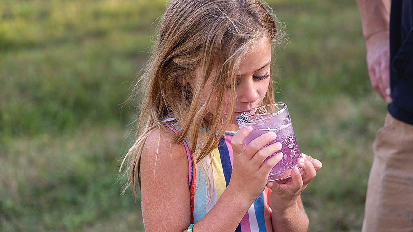 Child drinking a purple beverage from a glass outdoors.