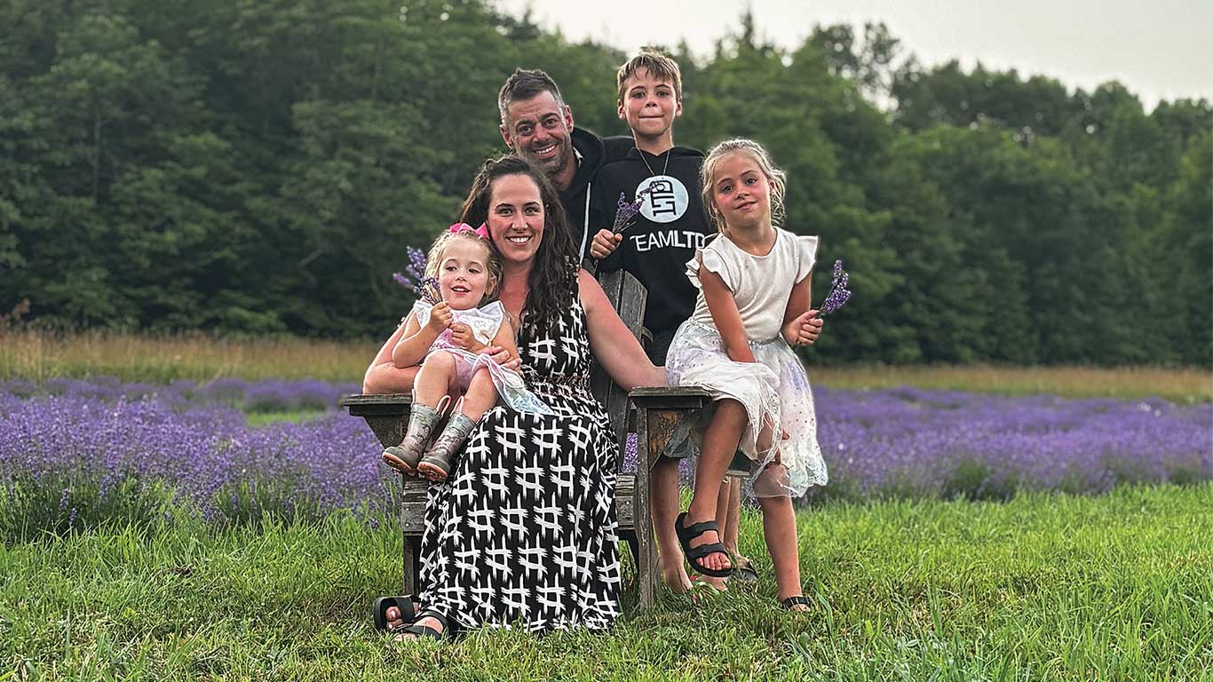 Group of people seated and standing in a lavender field holding flowers.