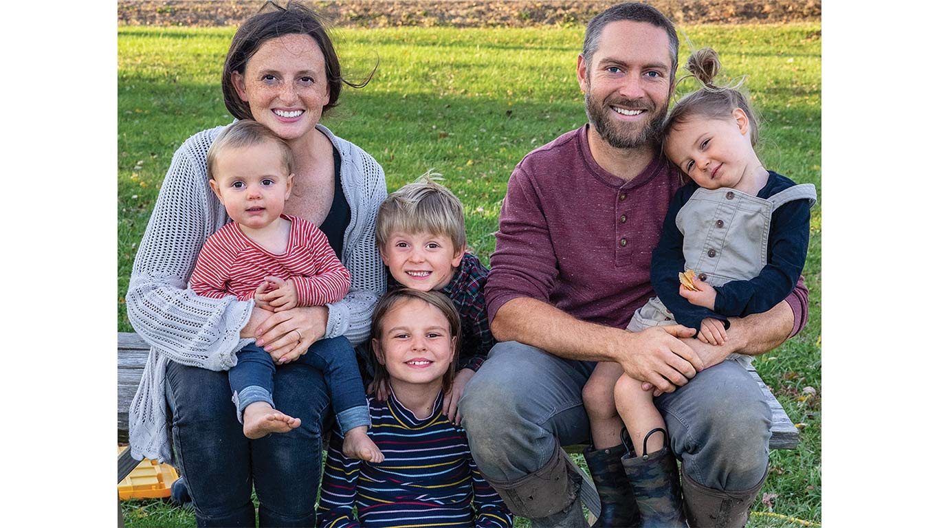 Family sitting outdoors on a bench in a grassy area.