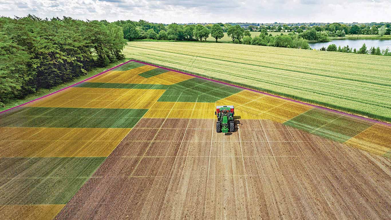 Aerial view of patchwork crop field with tractor in center, surrounded by varied plot sections.
