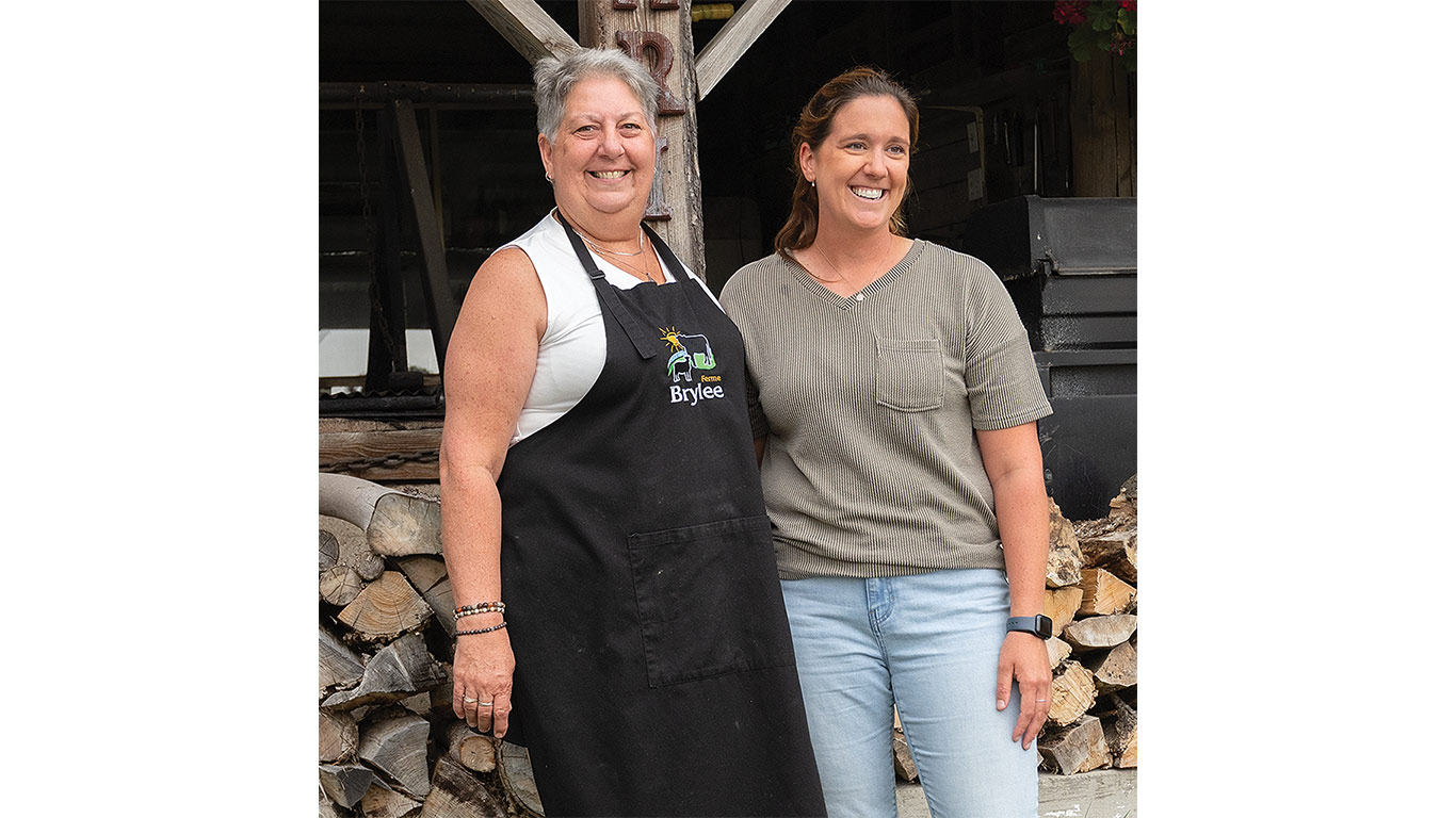 Two individuals posing in front of a barn and logs.