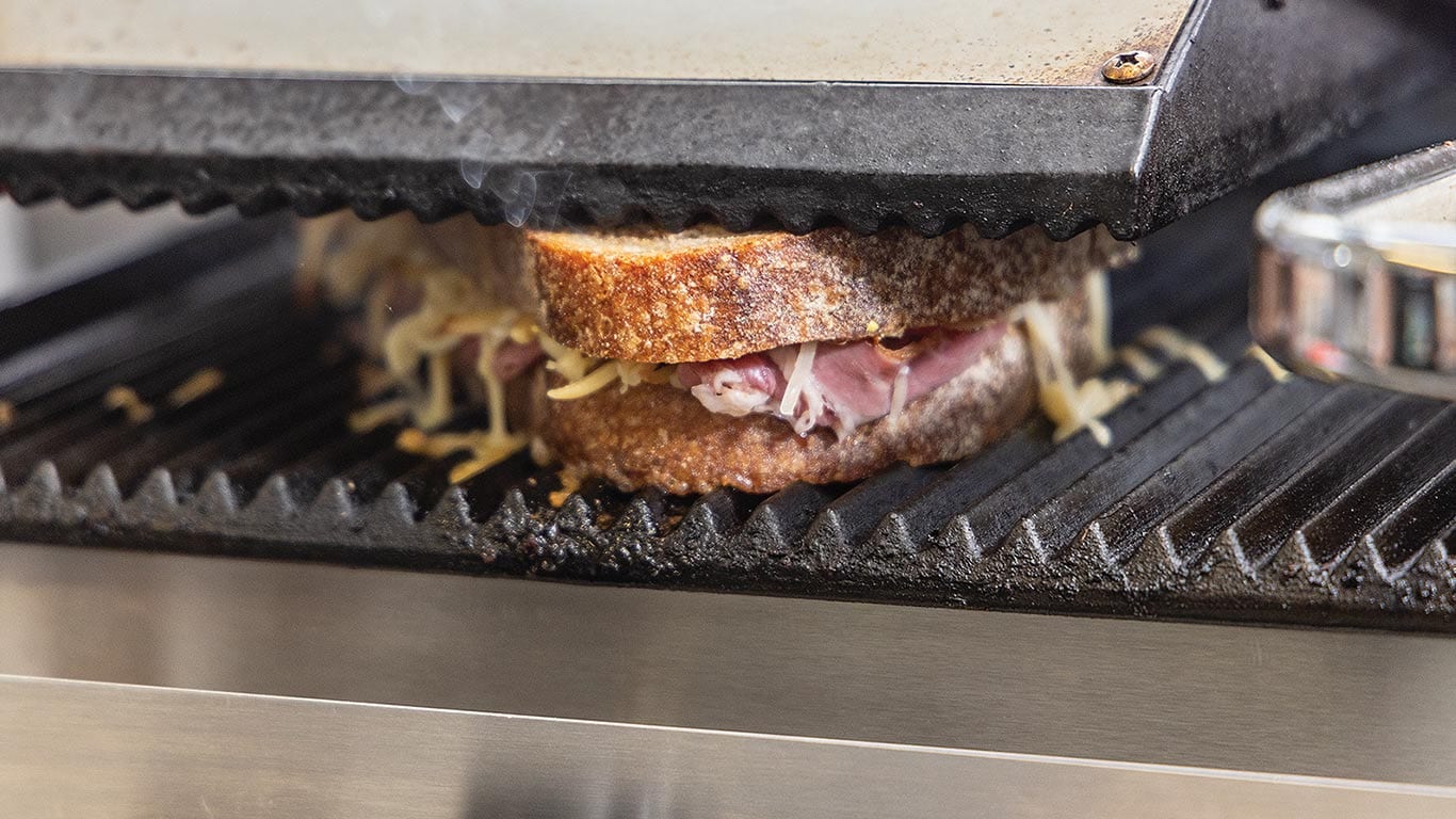 A reuben sandwich on a grill being pressed down to add grill marks to both sides of the bread.