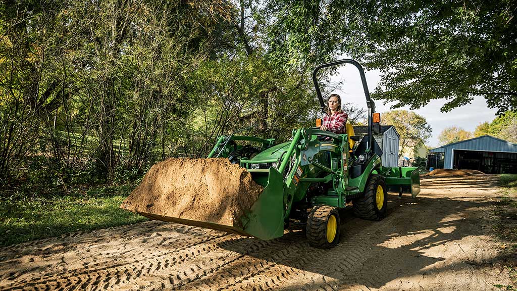 woman riding a compact utility tractor with a loader full of dirt