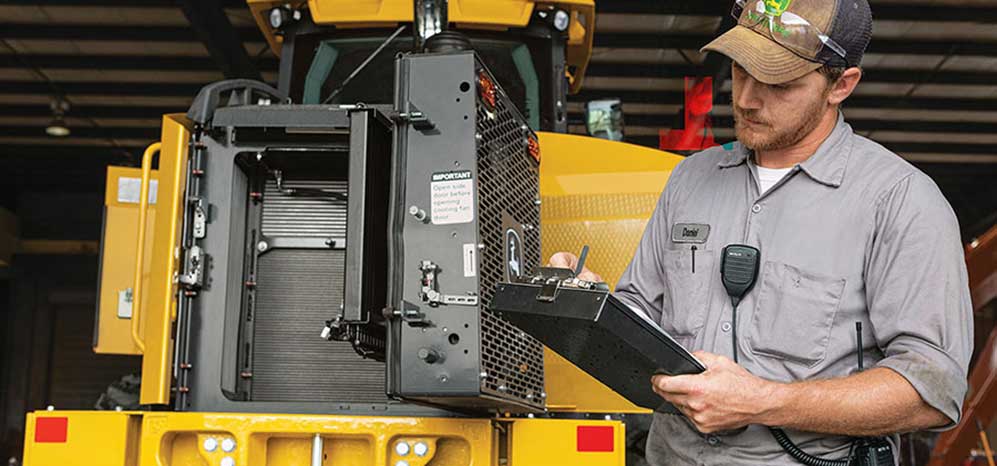Technician evaluates a wheel loader machine with a clipboard and pen in hand